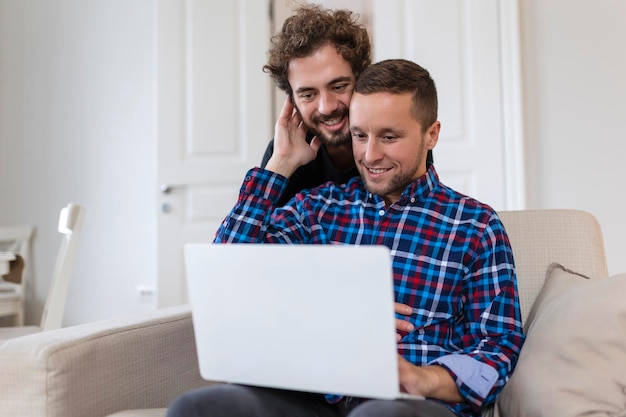 Lovely gay couple laughing together while sitting in their\
living room at home two romantic young male lovers having fun\
surfing the internet indoors young gay couple living together