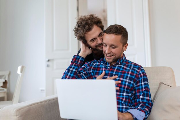 Lovely gay couple laughing together while sitting in their
living room at home two romantic young male lovers having fun
surfing the internet indoors young gay couple living together