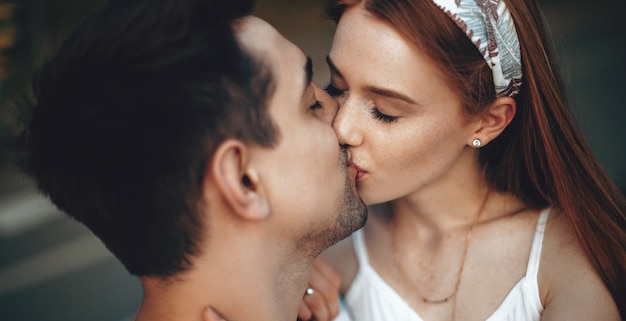 Photo lovely ginger woman with freckles kissing her lover while having a walk in the park