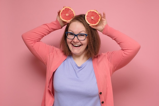 Lovely girl holding a slice of grapefruit in front of her face and smiling