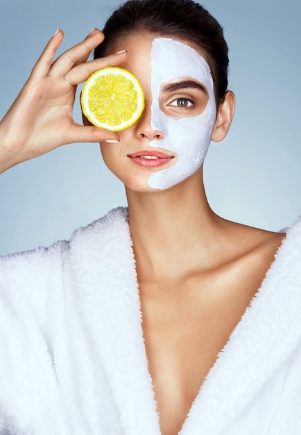 Lovely girl holding a slice of lemon in front of her face and smiling