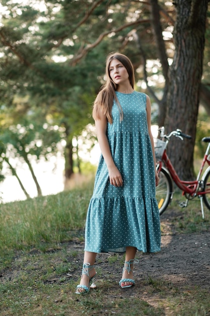 Bella ragazza in abito estivo su strada forestale con la bicicletta