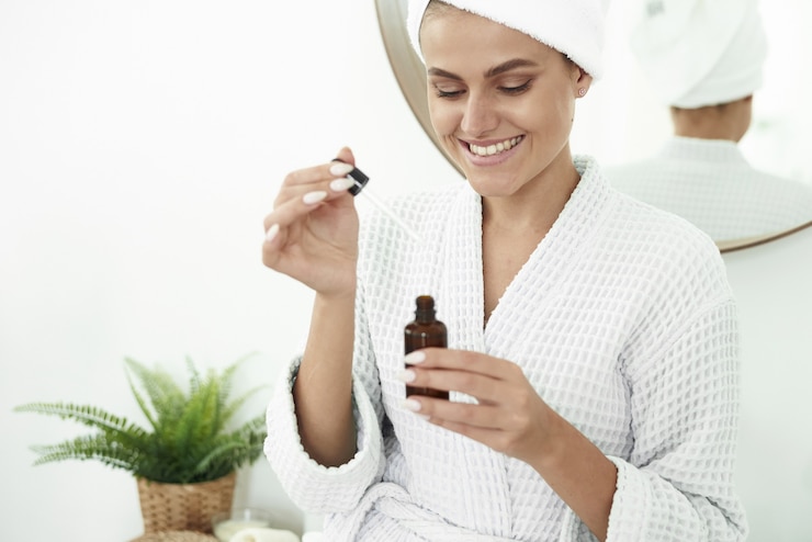 Lovely girl with vitiligo smiles with a snow-white smile using moisturizing serum. Close up of a dropper from a pipette on the background of hands.