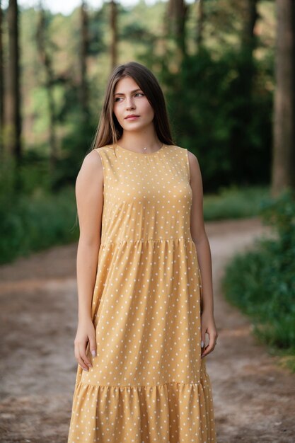 Lovely girl in yellow summer dress on forest road