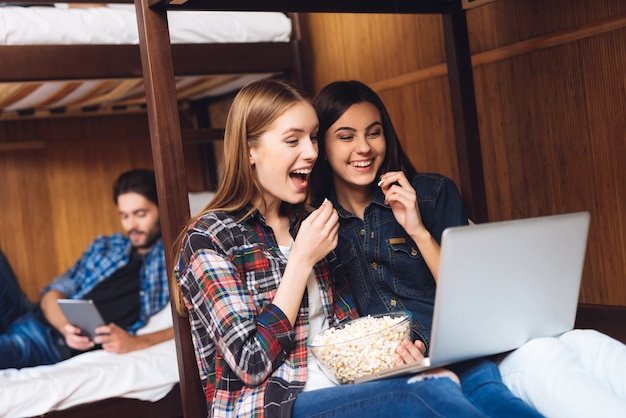 Lovely girls sit on bed and watching movie together.