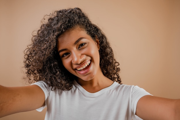 Lovely happy black young woman making selfie isolated over brown