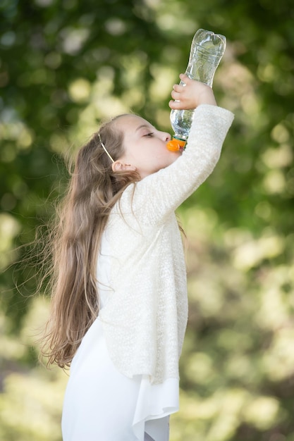 Lovely happy little girl drinking water at summer day