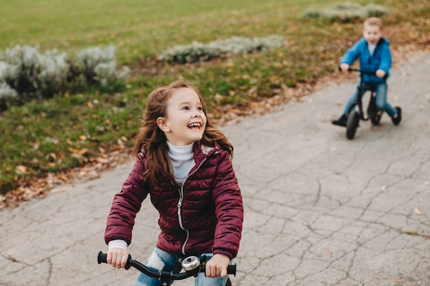 Foto bella bambina felice guardando i suoi genitori che ridono mentre va in bicicletta nel parco con suo fratello.