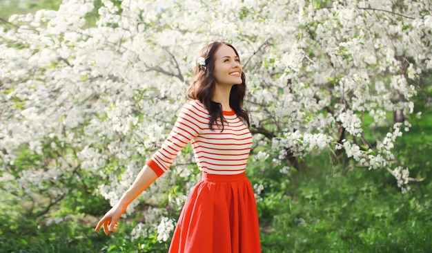 Lovely happy smiling young woman in spring blooming garden with flowers on the trees in park