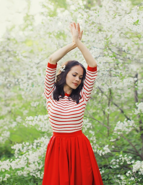 Lovely happy smiling young woman in spring blooming garden with white flowers on the trees in park