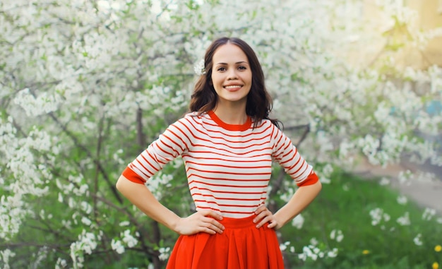 Lovely happy smiling young woman in spring blooming garden with white flowers on the trees in park