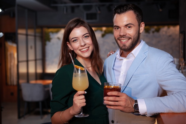 lovely happy young couple smiling to the camera, holding their cocktails at night club