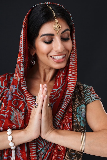 Lovely hindus girl in traditional indian saree dress and jewelry dancing with palms together isolated over black wall