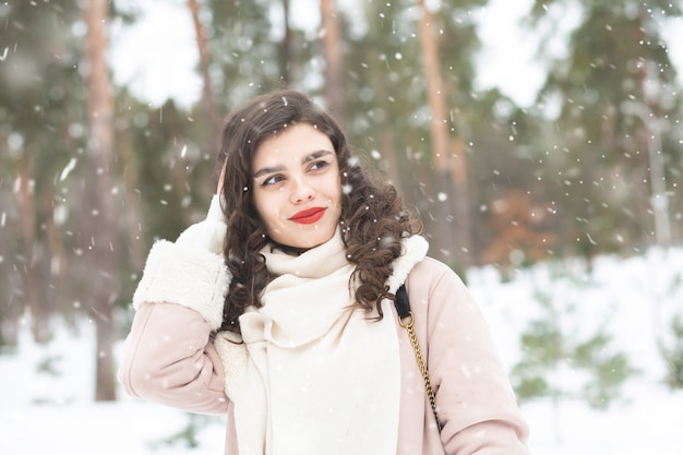 雪の降る天気で森の中を歩く長い髪の素敵な女性