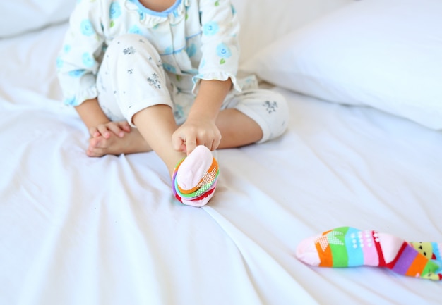 Lovely little asian girl trying to put a socks on the bed.