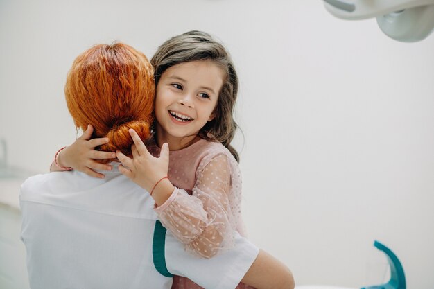 Lovely little girl embracing her doctor after teeth surgery .