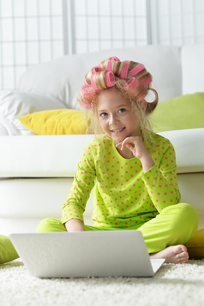 Lovely little girl with pink curlers using laptop