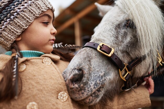 Lovely little pony snuggling up to cute Caucasian girl horizontal close up shot