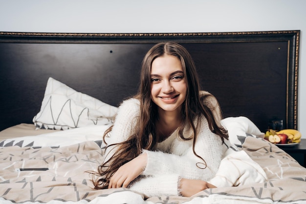Lovely longhaired girl is lying in bed late at night resting after a work day and smiling
