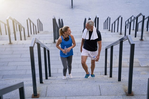 Lovely mature couple man and woman in sportswear smiling at each other walking up the stairs after