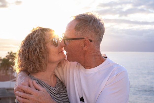 Lovely mature romantic senior couple embrace at sunset on the seashore expressing love