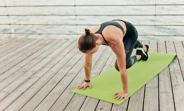 Lovely muscular sportswoman in sportswear performance her body and doing exercises on the beach terrace. Outdoor sports