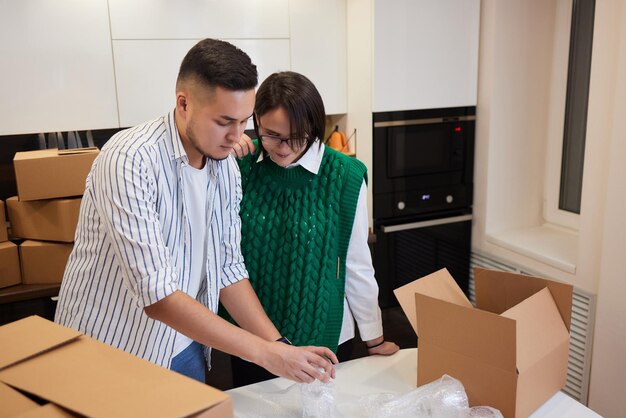 Lovely newlyweds with cardboard boxes moving in new apartment\
standing together on kitchen while man