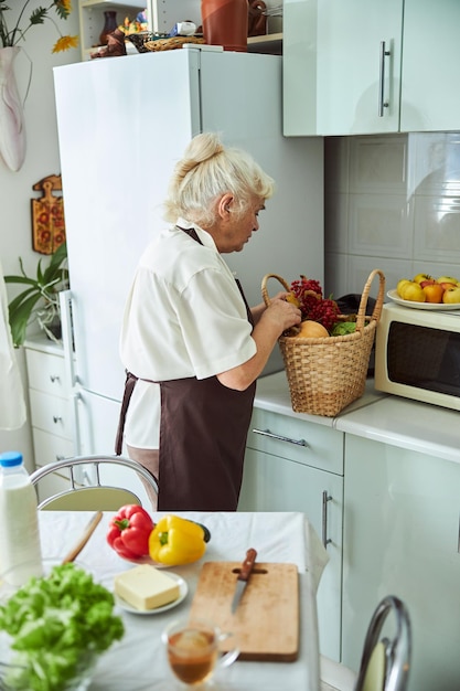 Прекрасная пожилая женщина проверяет корзину с продуктами на кухне