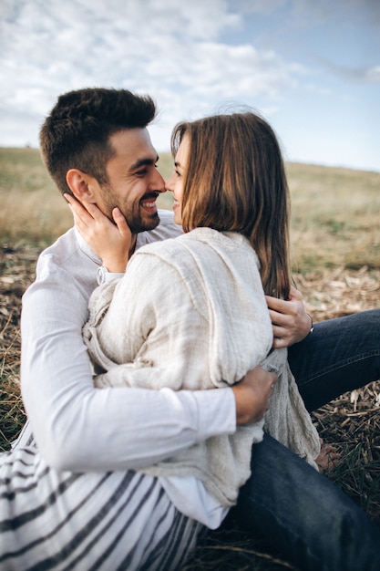Фото Прекрасная пара обниматься, целоваться и улыбаться на фоне неба, сидя на траве. портрет крупным планом