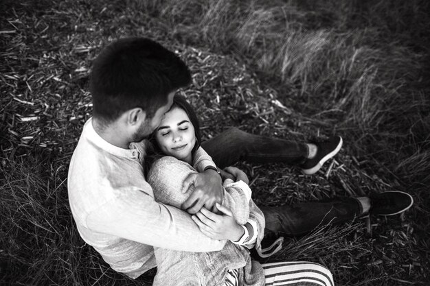 Lovely Сouple hugging, kissing and smiling against the sky seating on grass. Close up portrait