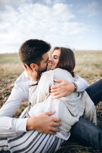 Foto bella coppia che si abbraccia, si bacia e sorride contro il cielo seduti sull'erba. spazio per il testo