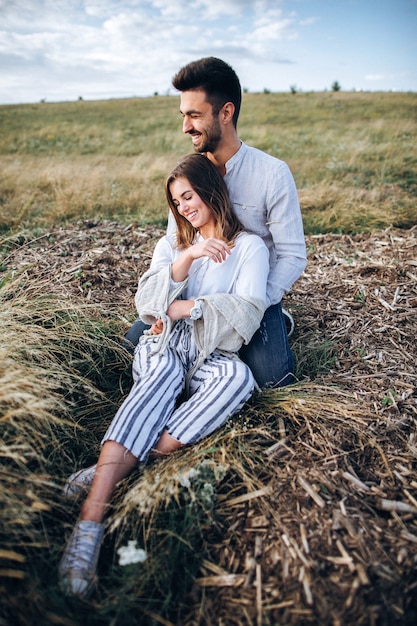 Lovely Сouple hugging, kissing and smiling against the sky seating on grass