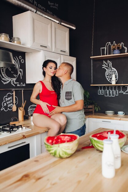 Photo lovely pair expecting little baby caring husband kissing beautiful pregnant wife while cooking dinner at kitchen future parents touching belly and hugging each other concept of pregnancy