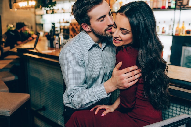 Maschera adorabile dell'uomo bello e di bella donna che si siedono molto vicino insieme. la tiene sulle sue mani e sta provando a baciarla. sta sorridendo e non se ne preoccupa.