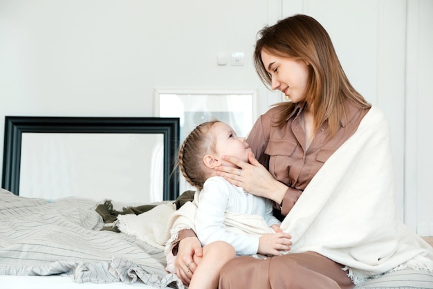 Lovely portrait of mother and daughter A little girl hugs her mother in a bright bedroom An adult woman enjoys love from her daughter Mothers Day