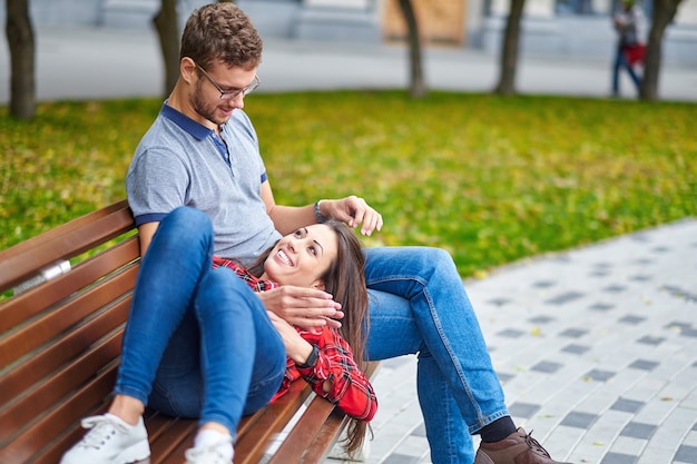 若いカップルの素敵なポートレート。彼らはベンチに座って抱き合い、キスをしています。