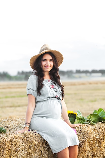 Lovely pregnant woman next to the hay bale in the sunlight