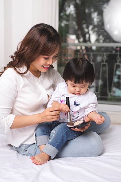 L'adorabile principessa sta applicando il trucco sulla sua pelle con un pennello speciale perché vuole assomigliare a sua madre adulta