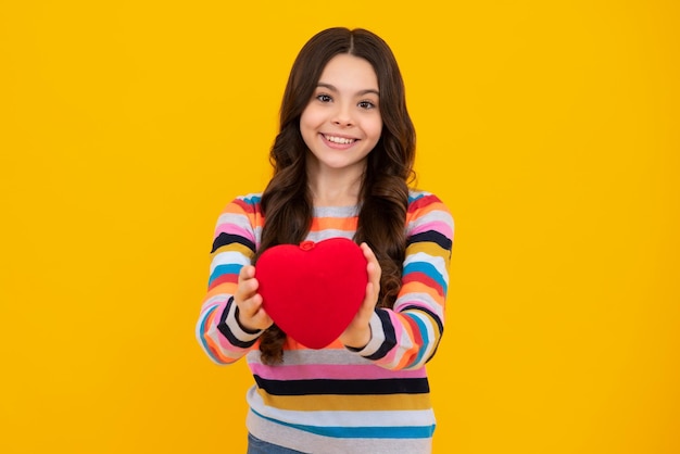 Foto bella ragazza adolescente romantica tenere il cuore rosso simbolo dell'amore per il giorno di san valentino isolato su sfondo giallo felice adolescente emozioni positive e sorridenti della ragazza adolescente