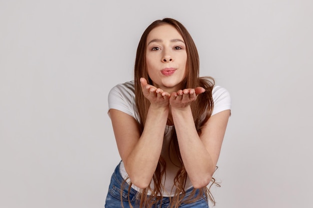 Lovely romantic woman looking at camera sending air kissing over palms hands expressing love