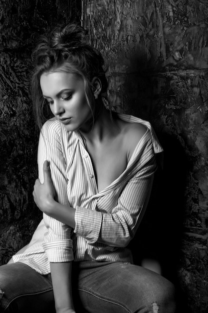 Lovely sad brunette woman with natural makeup wears shirt posing at studio. Black and white portrait