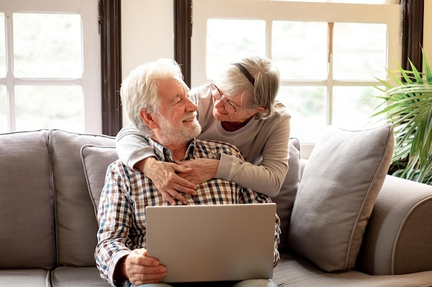 Lovely senior couple relax on sofa in living room enjoying retirement and free time browsing on laptop Older generation and wireless technology users concept