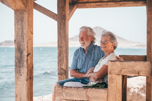 Lovely senior family couple sitting close to the beach looking at horizon over sea enjoying vacation