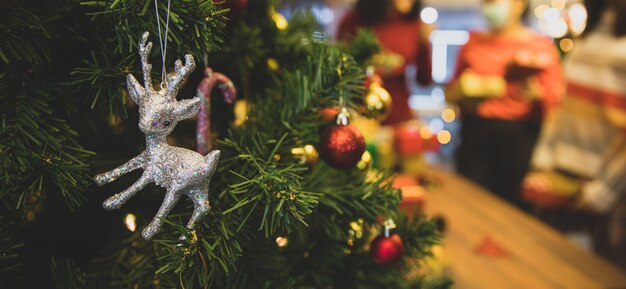 Lovely silver reindeer doll and beautiful ornament ball hang on Christmas tree as Santa decoration for shiny night party at home in winter holiday festival. Add some noise to fit vintage-style image