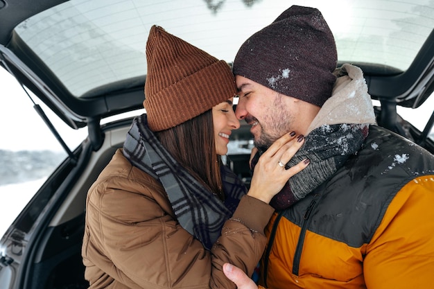 Bella coppia sorridente seduta nel bagagliaio di un'auto nella foresta invernale