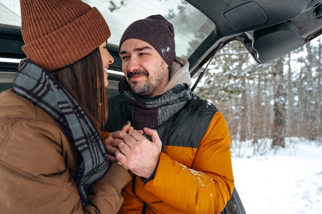 Lovely smiling couple sitting in car trunk in winter forest