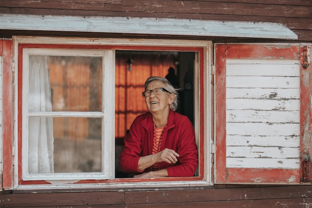 Lovely, smiling grandmother watching out of the window and enjoying sunny day,  a retirement life