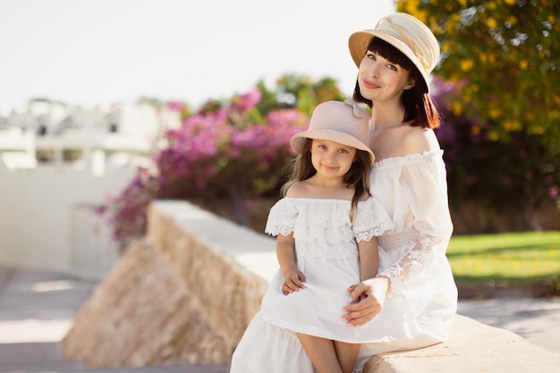 Lovely smiling lady with her daughter posing with straw hat sitting on blur background