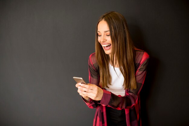 壁に携帯電話を使用して素敵な笑顔の若い長い髪の女性
