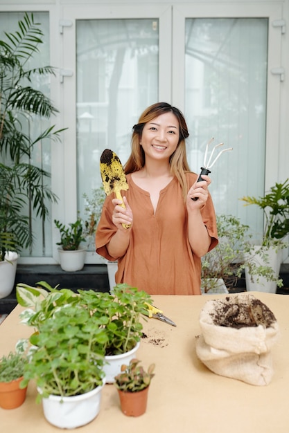 手こてと植物の植え替えの準備ができて園芸フォークで立っている素敵な笑顔の若い女性